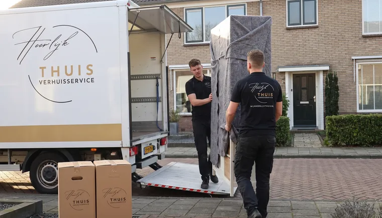 Twee verhuizers van Heerlijk Thuis dragen een in dekens gewikkelde kast naar de verhuiswagen